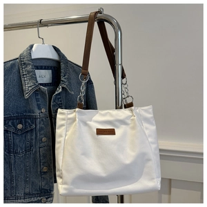 Detail of white tote bag with brown leather strap and silver metal chain accents