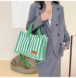 Detail of green and white striped canvas tote bag featuring brown leather fashion label