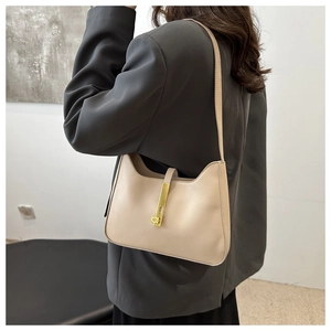 Detail of a beige leather underarm bag with a golden metal clasp worn with a grey blazer