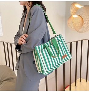 Detailed close-up of green striped canvas tote bag with adjustable strap and leather patch