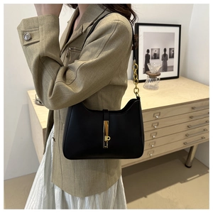 Detail of black leather hobo bag with gold metal clasp and chain strap on model
