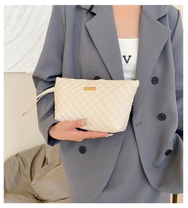 Close-up of cream quilted lattice clutch bag with gold logo plate and top handle strap