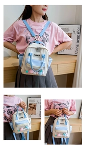 Dettaglio dello zaino in nylon bianco e blu con tasca in PVC trasparente e pompon colorati