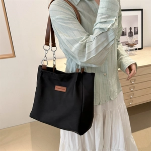 Minimalist black nylon tote bag with brown leather straps and silver metal chain detail