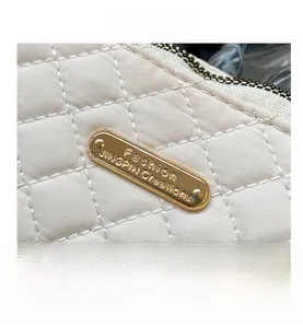 Detail of quilted rhombic stitching and golden oval metal logo on a beige clutch bag