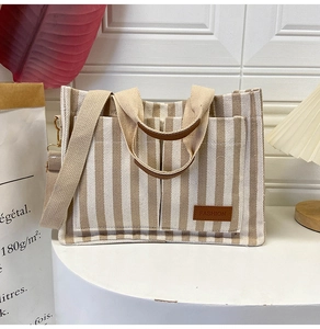 Detail of striped canvas tote bag with front pockets and fashion leather label on desk