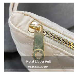 Macro shot of gold metal zipper pull and quilted diamond pattern on beige handbag