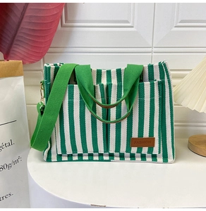 Detail of green and white striped canvas tote bag with front pockets and fashion logo