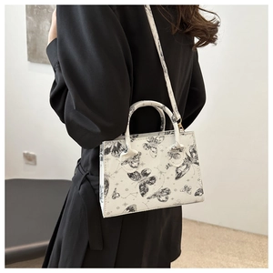 Détail du sac cabas blanc en cuir à imprimé papillon porté par un mannequin en robe noire