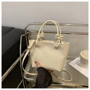 Detail of creamy white bucket bag with pebble leather texture and rope knot handle