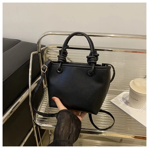 Detail of black lychee pattern leather bucket bag with stylish knotted handle and gold hardware