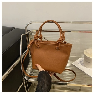 Detail of caramel lychee grain leather bucket bag featuring decorative knot handles and strap