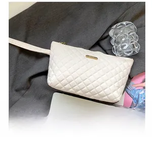 Close-up of quilted white clutch with gold logo plate and matching wristlet strap