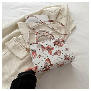 Detail of white shoulder bag with butterfly print and adjustable strap on a cream blazer
