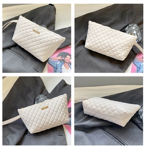 Detail view of white quilted cosmetic bag with gold zipper and metal nameplate in urban setting