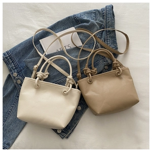 Detail of minimalist bucket bags in beige and brown with knotted handle and cross-body strap