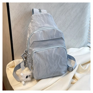 Détail d'un sac bandoulière gris en nylon froissé avec zips et pendentif peluche