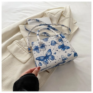 Detail of a white square shoulder bag with blue butterfly prints and round handles