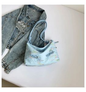 Close-up of light blue shoulder bag with textured fabric, embroidery, and bow details