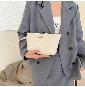 Close-up of beige quilted clutch bag with diamond stitching and gold metal logo plaque