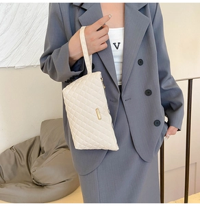 Detail of beige quilted clutch bag with wrist strap and gold metal plate for women