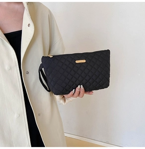 Detailed view of black quilted clutch bag with gold zipper and metal fashion logo plate