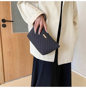 Detail of black quilted clutch with classic diamond stitching and gold logo plaque