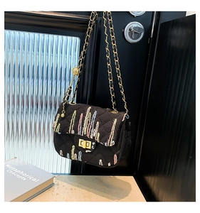 Detail of a black quilted leather bag with vertical embroidery and a gold turn-lock