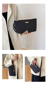 Detail of black quilted envelope clutch with golden metal logo and nylon texture