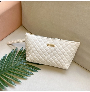 Close-up of white quilted handbag with golden Fashion logo plate and zipper detail
