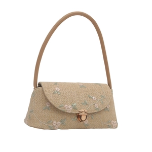 Straw shoulder bag with floral lace embroidery and gold metal clasp closure on white background