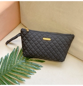 Detail of black quilted pouch with golden Fashion emblem and zipper closure