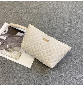 Detail of quilted rhombic stitching and gold 'Fashion' metal plate on off-white clutch bag