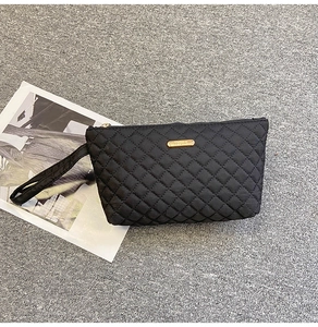 Detail of black quilted envelope clutch bag with gold plaque and wrist strap