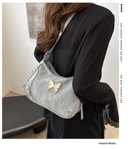 Détail d'un sac porté épaule gris clair avec boucle papillon argentée et texture marbrée