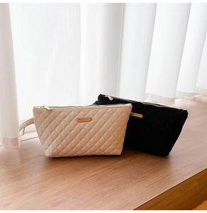 Close-up of quilted ivory and black toiletry bags with gold logo and zip detail