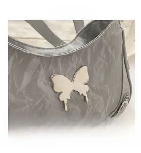 Détail du logo papillon argenté et de la texture froissée du sac à bandoulière gris