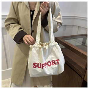 Detail of a beige canvas tote bag with red SUPPORT text and drawstring closure