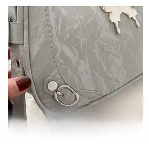 Détail du sac à bandoulière gris texturé avec pendentif papillon et boucle en argent