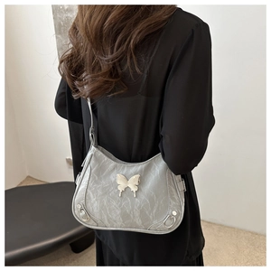 Détail d'un sac bandoulière gris clair avec papillon argenté et texture plissée