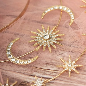 Detailed close-up of golden sun and moon headpiece with rhinestones on pink lace