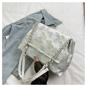 Detail of white satin shoulder bag featuring blue and gold butterfly embroidery and silver chain