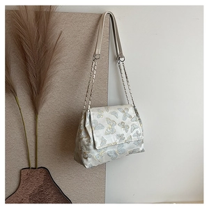 Detail of elegant butterfly embroidery and silver chain strap on cream shoulder bag