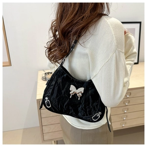 Détail d'un sac bandoulière noir plissé avec papillon argenté et boucles métalliques