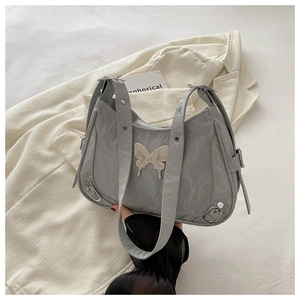 Détail d'un sac plissé gris avec décoration papillon en métal et bandoulière à œillets