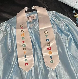 Detail of light blue satin kindergarten graduation gown and sash with rainbow lettering