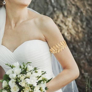 Golden leaf upper arm cuff bracelet in Greek style worn by a bride with a bouquet