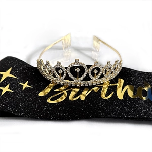 Close-up of sparkling rhinestone birthday crown and black glitter sash with golden text
