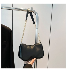 Detail of black faux leather underarm bag with gold chain strap and sleek zip closure