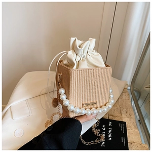 Detail of beige textured bucket bag with white pearl handle and gold chain strap